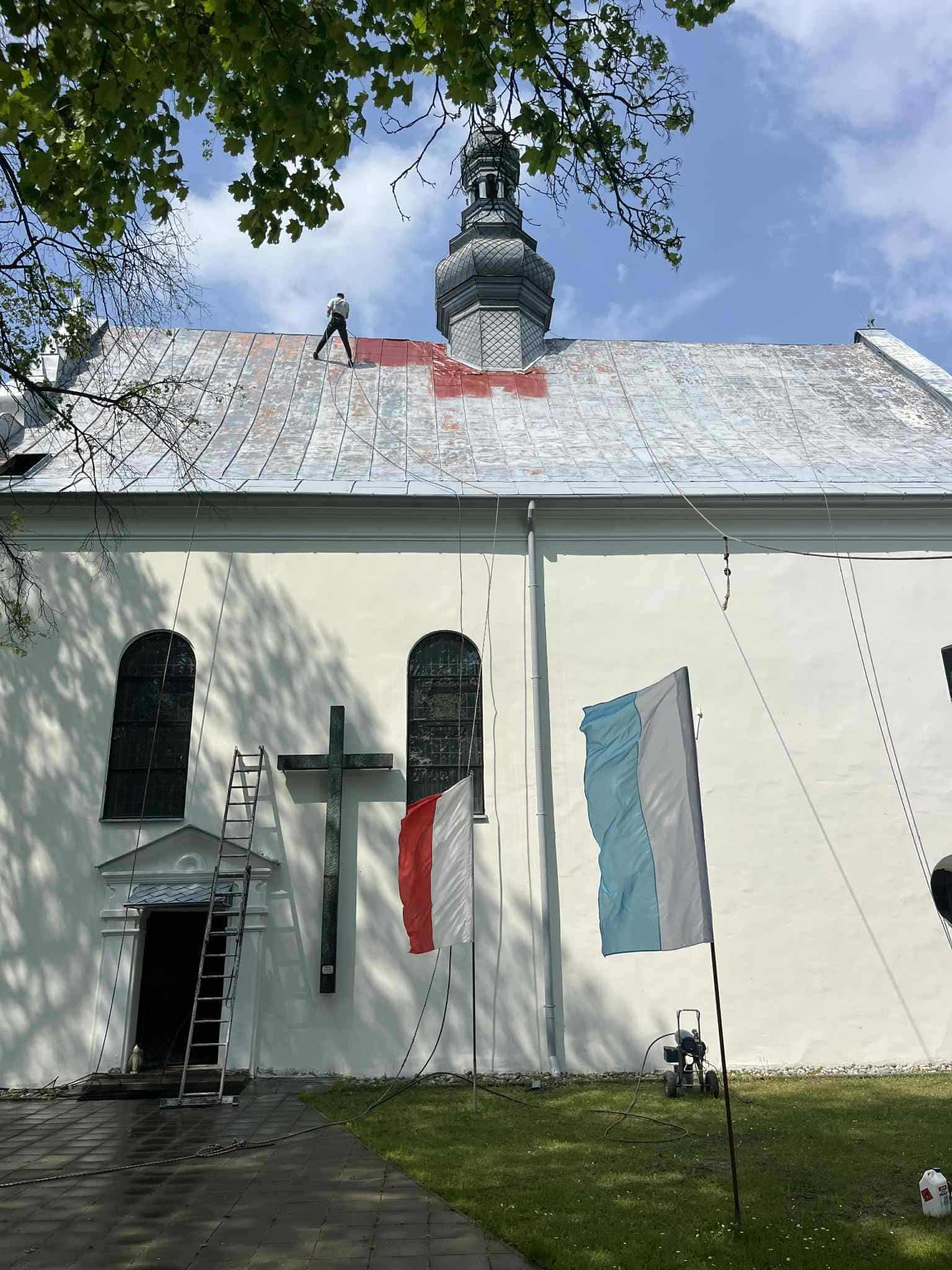 Malowanie dachu kościoła, pierwsze pasy czerwonej farby na starej blasze
